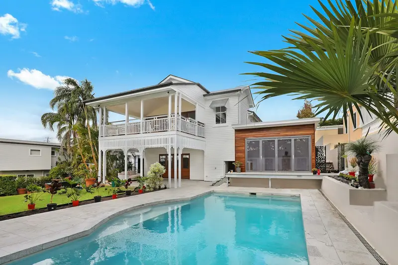White two story house with a rectangular swimming pool and palm trees