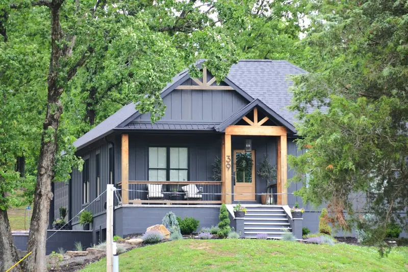 Dark gray house with a covered front porch among trees