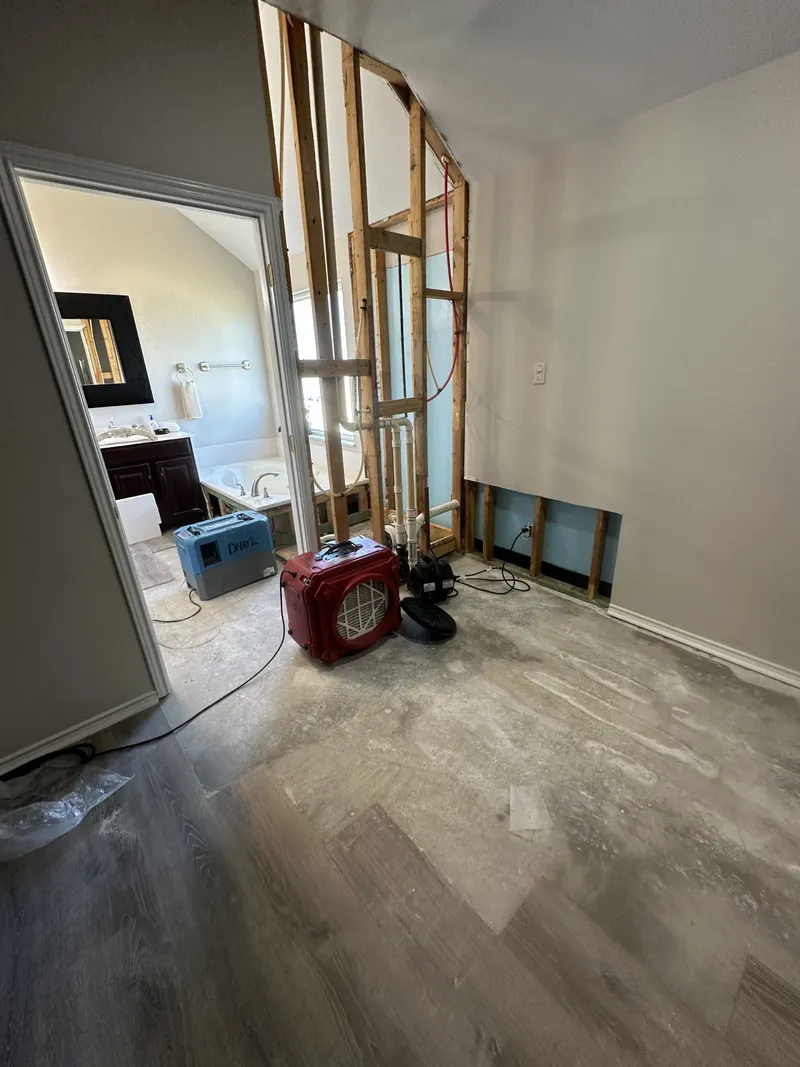 Air mover and dehumidifier drying an opened bathroom wall, with the flooring pulled up to the slab