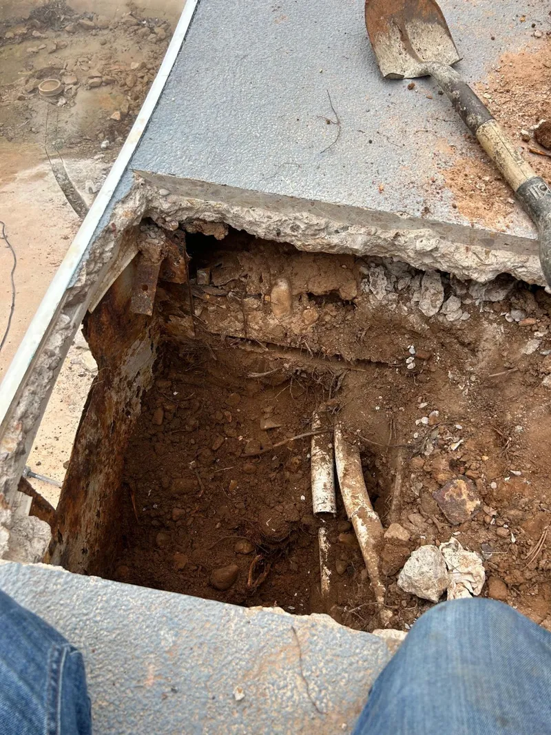 Opening cut in the pool deck behind the wall, showing the steel wall panel and PVC lines in red soil