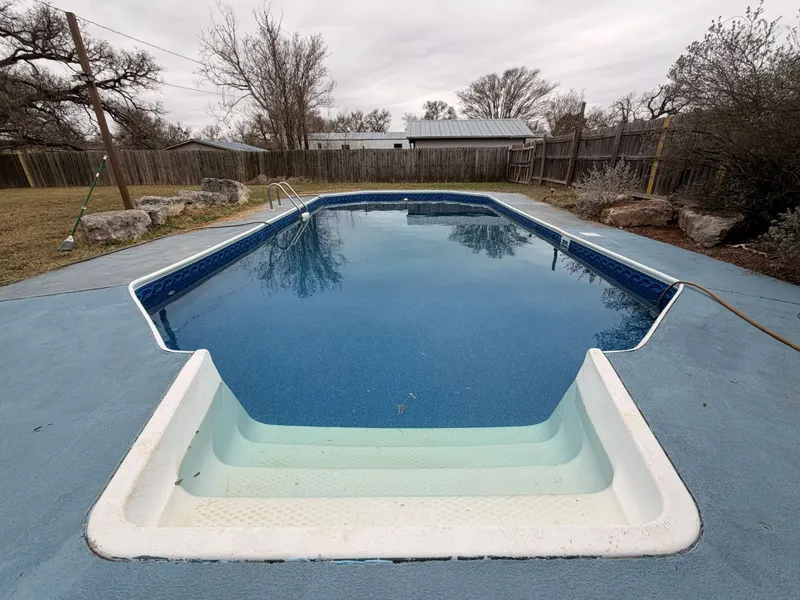 Finished vinyl liner pool full of water, with a blue patterned border, a stainless ladder and white entry steps